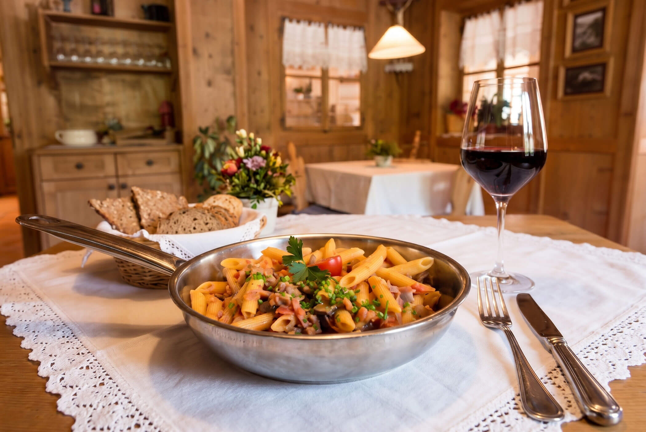 Eine Schüssel Pasta mit Brot und ein Glas Rotwein an einem hölzernen Esstisch in einem gemütlichen, rustikalen Raum. - Hotel Mooserhof