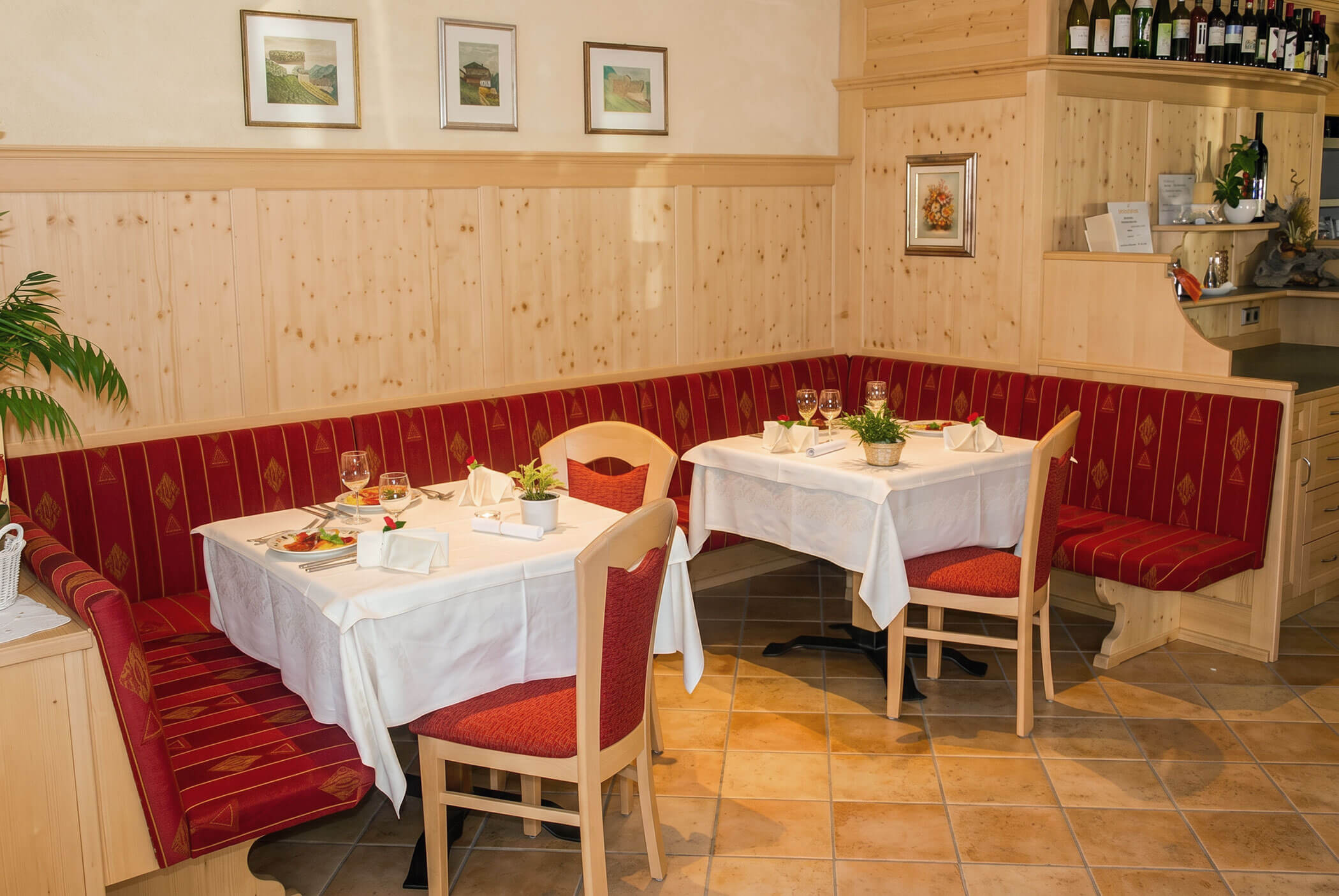 Gemütliche Restaurantecke mit roten Sitzpolstern, gedeckten Tischen und mit gerahmter Kunst dekorierten Holzwänden. - Hotel Mooserhof