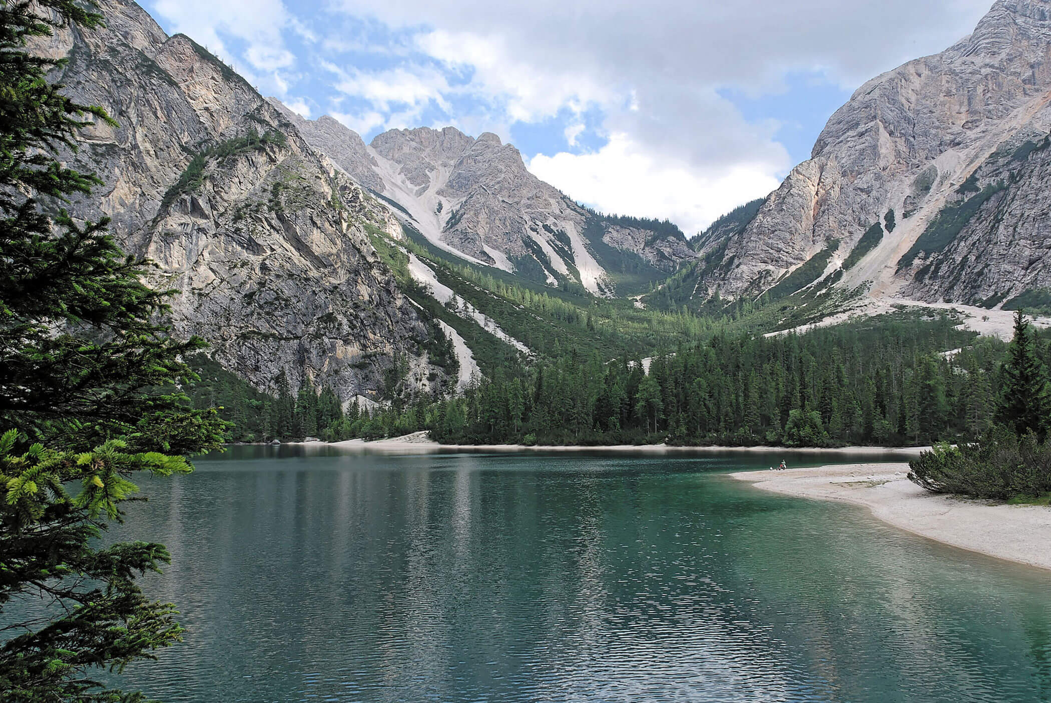 Ein klarer See, umgeben von Kiefern und hohen Felsen unter einem teilweise bewölkten Himmel. - Hotel Mooserhof